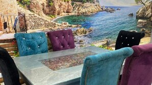 Ein Essbereich mit einer Wandmalerei einer Küstenlandschaft, einem Tisch mit Glasplatte und Samtstühlen in verschiedenen Farben.