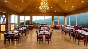 A spacious dining area with wooden floors and a high ceiling, featuring a chandelier and large windows offering mountain views. - Lemon Tree Hotel Mcleodganj (Dharamshala)