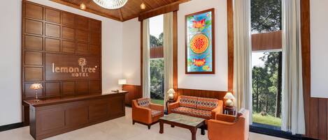 A hotel lobby with a reception desk, seating area, large windows, and a chandelier.