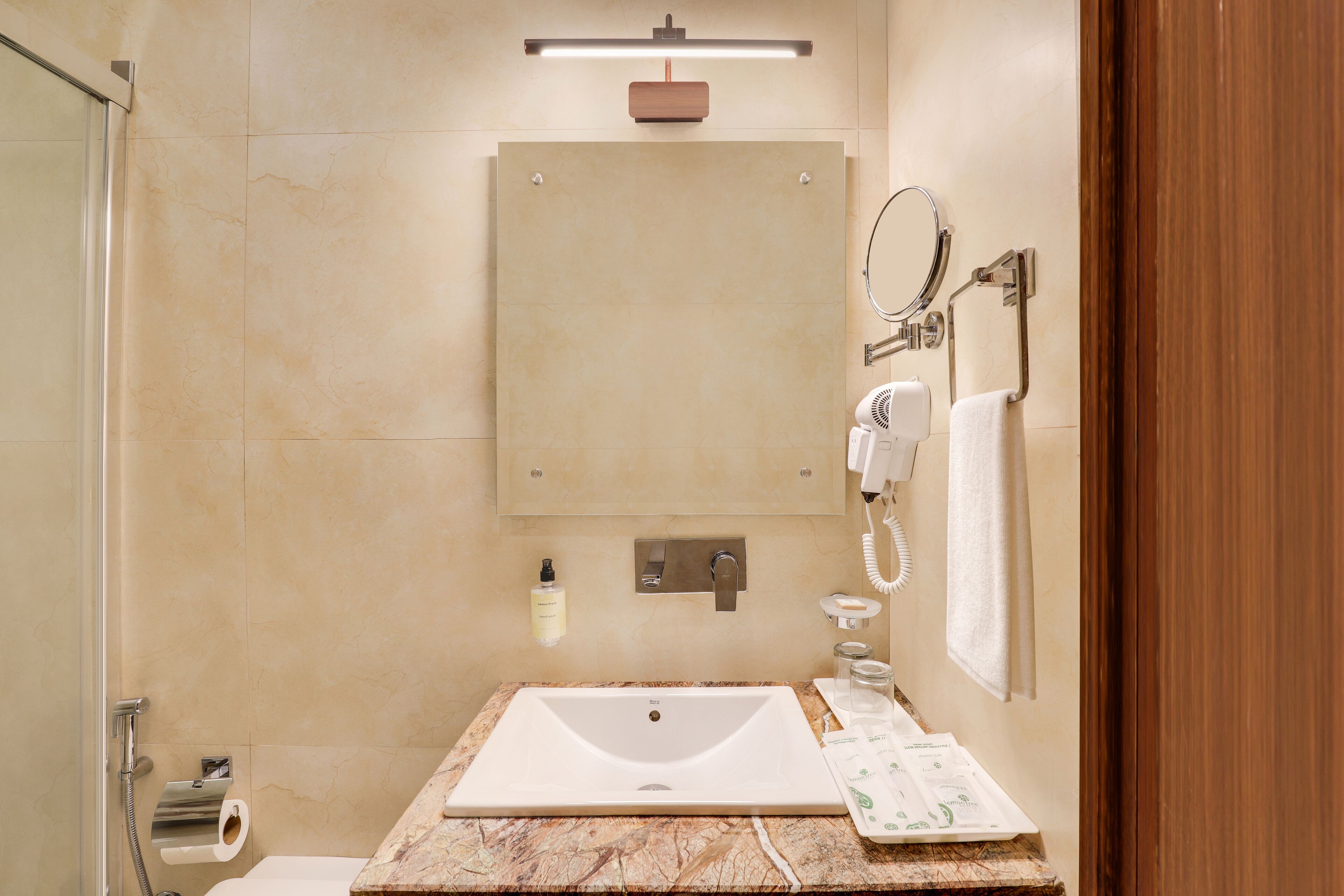 A modern bathroom with a marble sink, a handheld showerhead, a towel rack, and a mirror.
