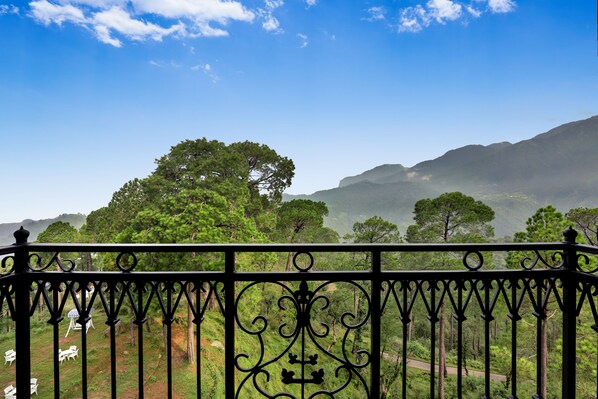 A balcony with wrought iron railings overlooking a lush landscape with trees and mountains.