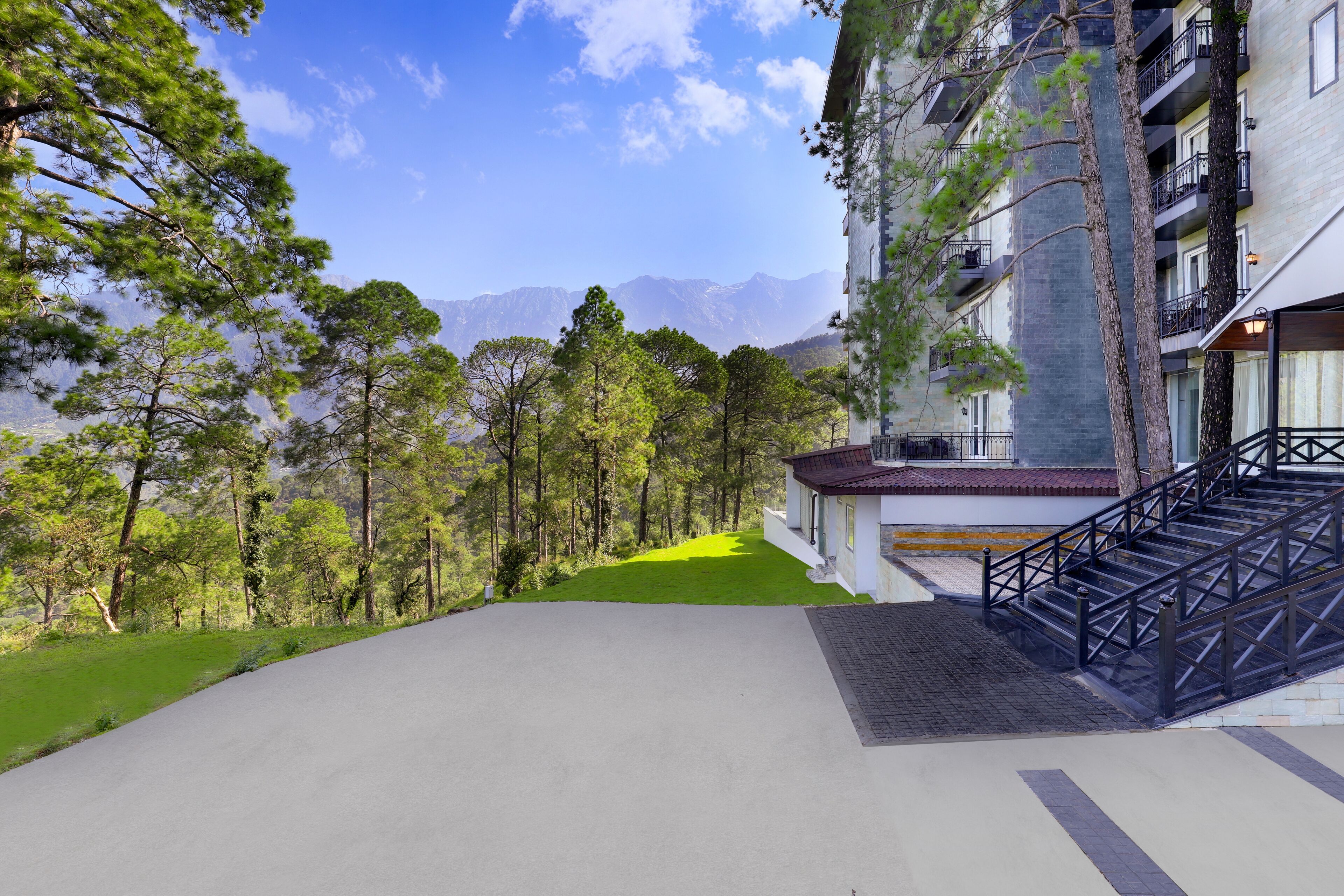 A hotel with a staircase leading to the entrance, surrounded by trees and a view of mountains.
