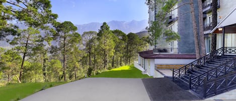 A hotel with a staircase leading to the entrance, surrounded by trees and a view of mountains.