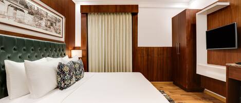 A modern bedroom with a large bed, wooden paneling, a mounted TV, and a framed picture on the wall.