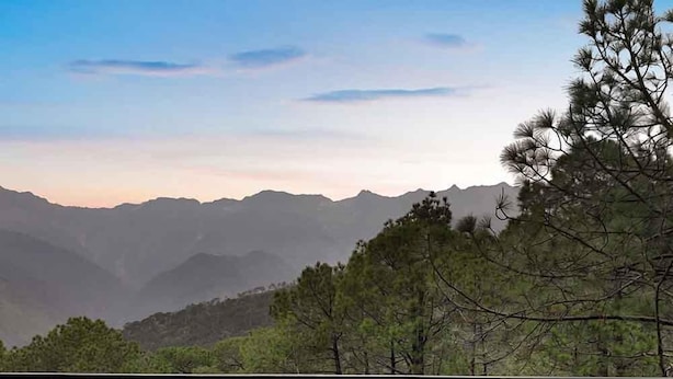 A balcony with wicker furniture and a table, overlooking a mountainous landscape. - Lemon Tree Hotel Mcleodganj (Dharamshala)