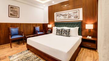 A hotel room with a large bed, two nightstands, a green upholstered headboard, and wooden paneling on the walls.