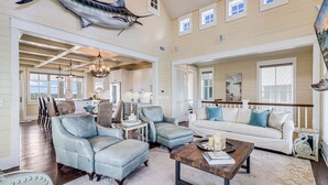 A spacious living room with a large sofa, two armchairs, a coffee table, and a dining area with striped chairs. - Stunning Lakeside Home near Keira’s Pool & More Cinnamon Shore Amenities. (Port Aransas)