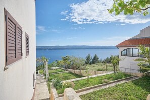 Una propiedad costera con vistas al mar, un jardín con un camino de piedra y un edificio blanco con contraventanas marrones.