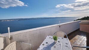Un balcone con tavolo e sedie, affacciato su una distesa d'acqua e una terraferma in lontananza.