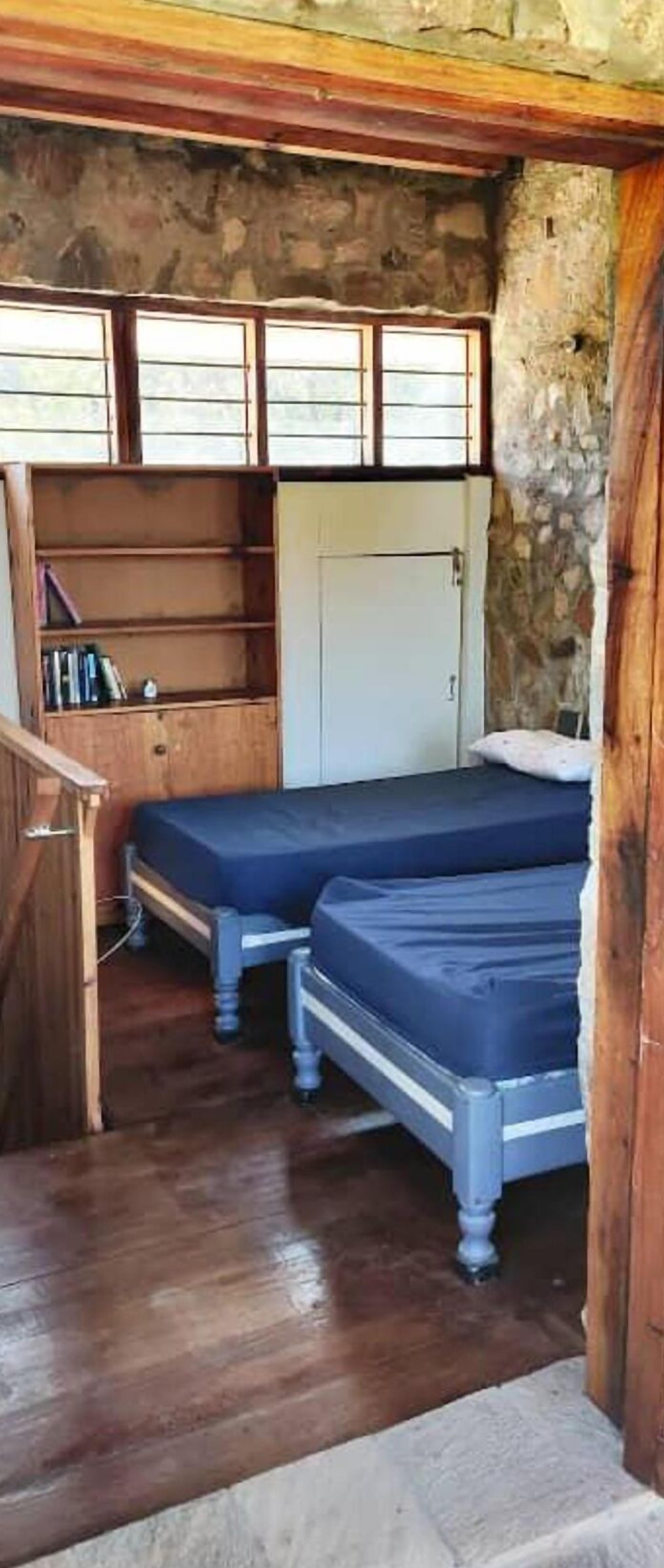 Une petite chambre rustique avec deux lits simples, un bureau en bois et un mur en pierre.