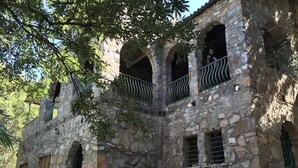 A stone building with arched windows and balconies, featuring outdoor seating and a small pool.