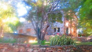 A stone building with a rustic appearance, surrounded by a stone wall and lush greenery.