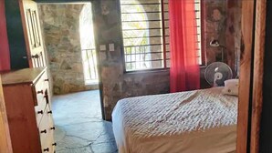 A room with a bed, a dresser, a window with bars, and a fan.