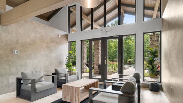 Un intérieur moderne avec un canapé, des fauteuils et une table basse. De grandes fenêtres offrent une vue sur l’extérieur.
