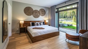 Une chambre moderne avec un grand lit, un bureau et une vue sur une forêt, visible à travers une porte vitrée.