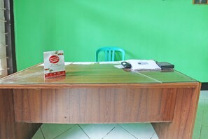A wooden desk with a glass top, a green chair, a telephone, and some papers.