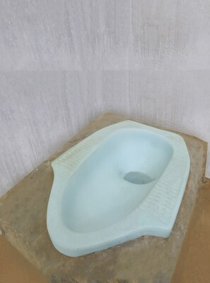 A simple, light blue squat toilet with a textured seat and a central hole, placed on a concrete platform against a plain wall.