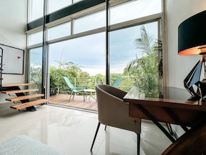 A modern room with a large sliding glass door leading to a balcony, a wooden desk, a chair, and a lamp. - Discover Luxury Living: Spacious 3-Bedroom Retreats at Azul Playacar! (PLAYA DEL CARMEN)