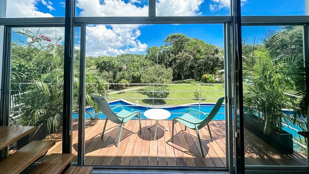 A view from a room with large windows overlooking a pool area with two green chairs and a table.
