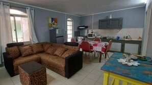 Ein Wohnzimmer mit einer Couch, einem Esstisch mit Stühlen, einer Küchenzeile mit Schränken und einer Mikrowelle sowie einem Ventilator.