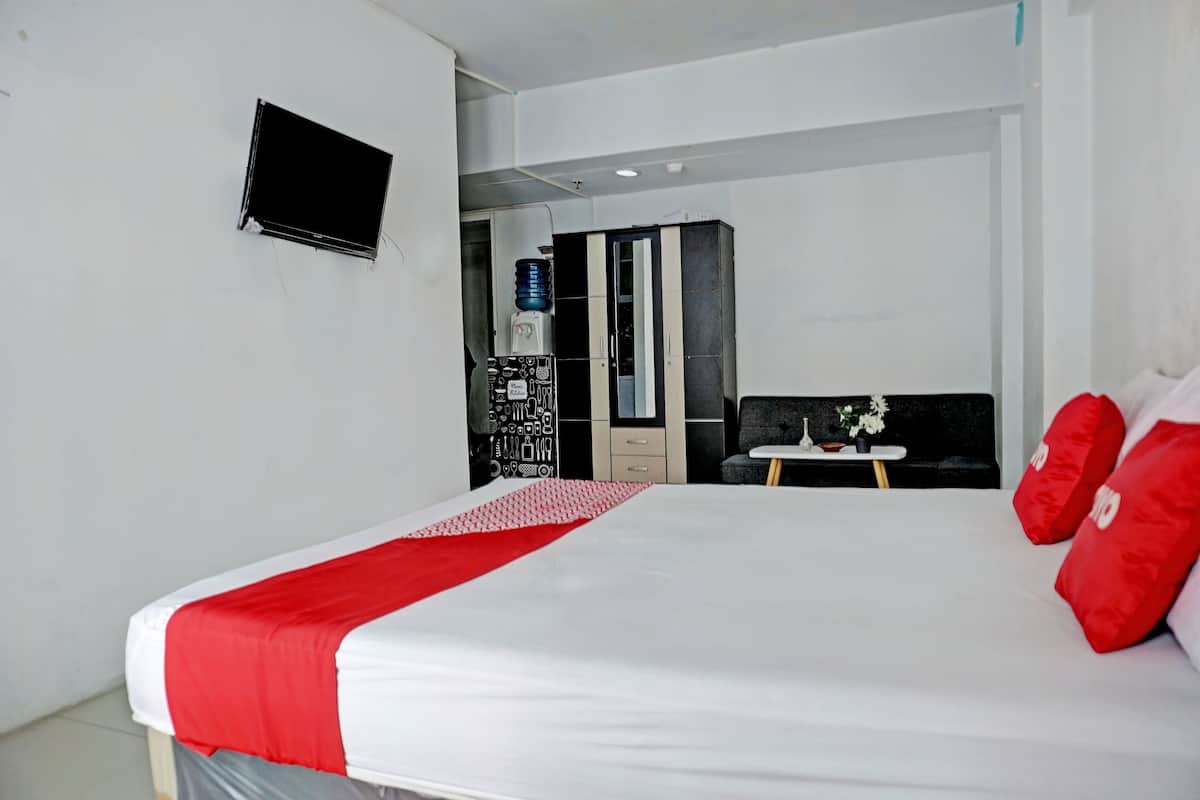 Quarto de hotel com uma cama grande, televisão na parede, guarda-roupa e uma pequena mesa com um vaso de flores.