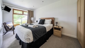 A hotel room with a bed, a chair, a bedside table, a wardrobe, a TV mounted on the wall, and a window with curtains. - Modern Peaceful Open Plan 1-bed Apartment Rutland (Oakham)
