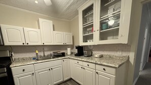 Una cocina con armarios blancos, encimera de granito, cafetera y tostadora.