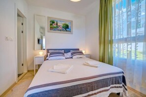 Une chambre à coucher avec un lit, deux tables de chevet, un tableau au mur et une fenêtre avec des rideaux.