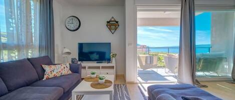 A modern living room with a sofa, a coffee table, a TV, and a balcony with a view.