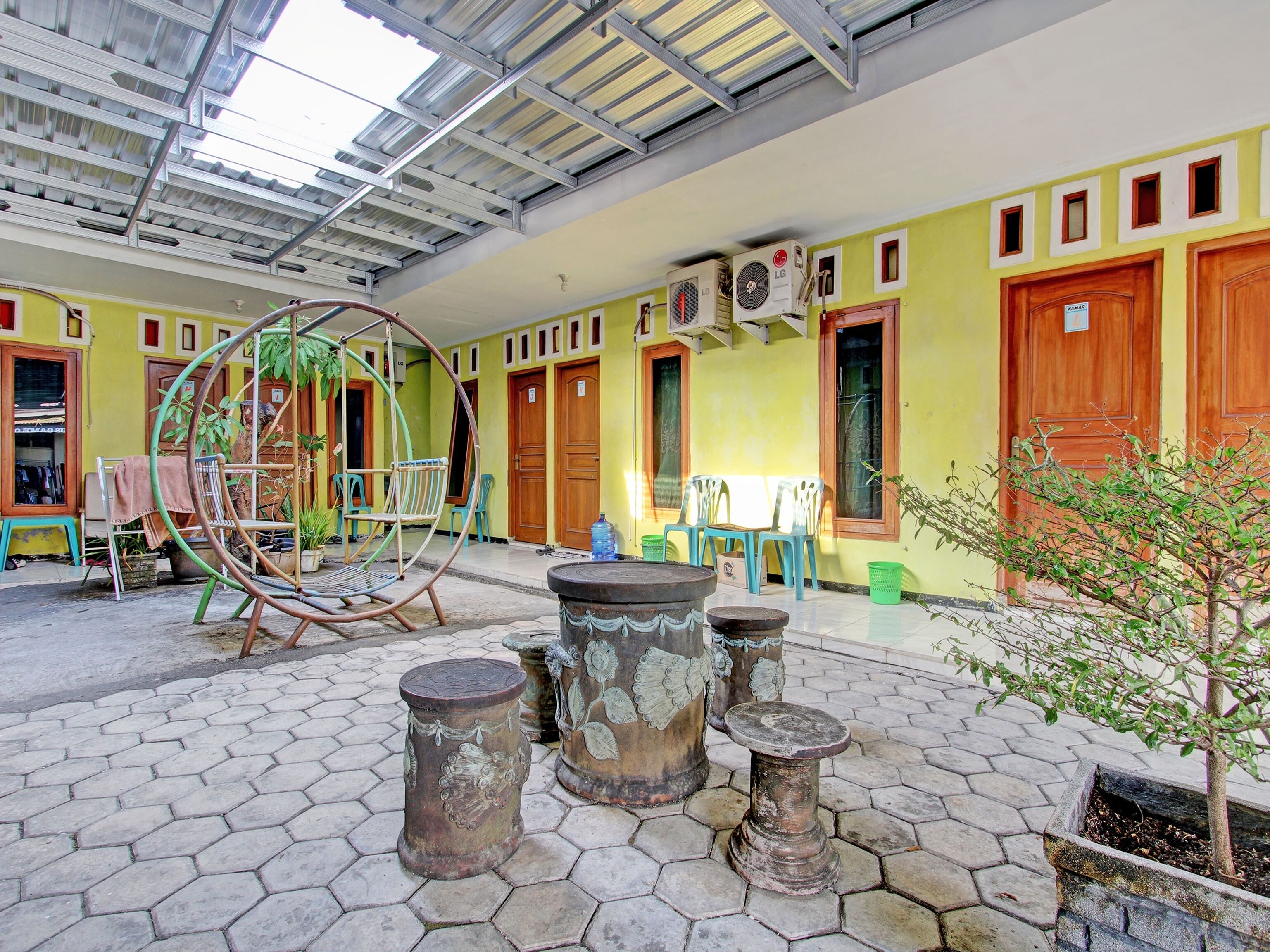 A spacious indoor area with a high ceiling, hexagonal tiled floor, and a swing chair. There are several plastic chairs and a small table.