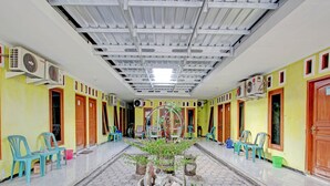 A corridor with tiled flooring, potted plants, and plastic chairs. - OYO 92998 Wiludjeng Guesthouse (Sragen)