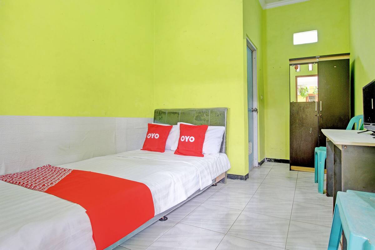 A room with two beds, each with red and white bedding, and a desk with a chair.