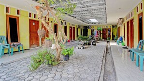 A covered outdoor area with hexagonal tiles, wooden doors, and plastic chairs. - OYO 92998 Wiludjeng Guesthouse (Sragen)