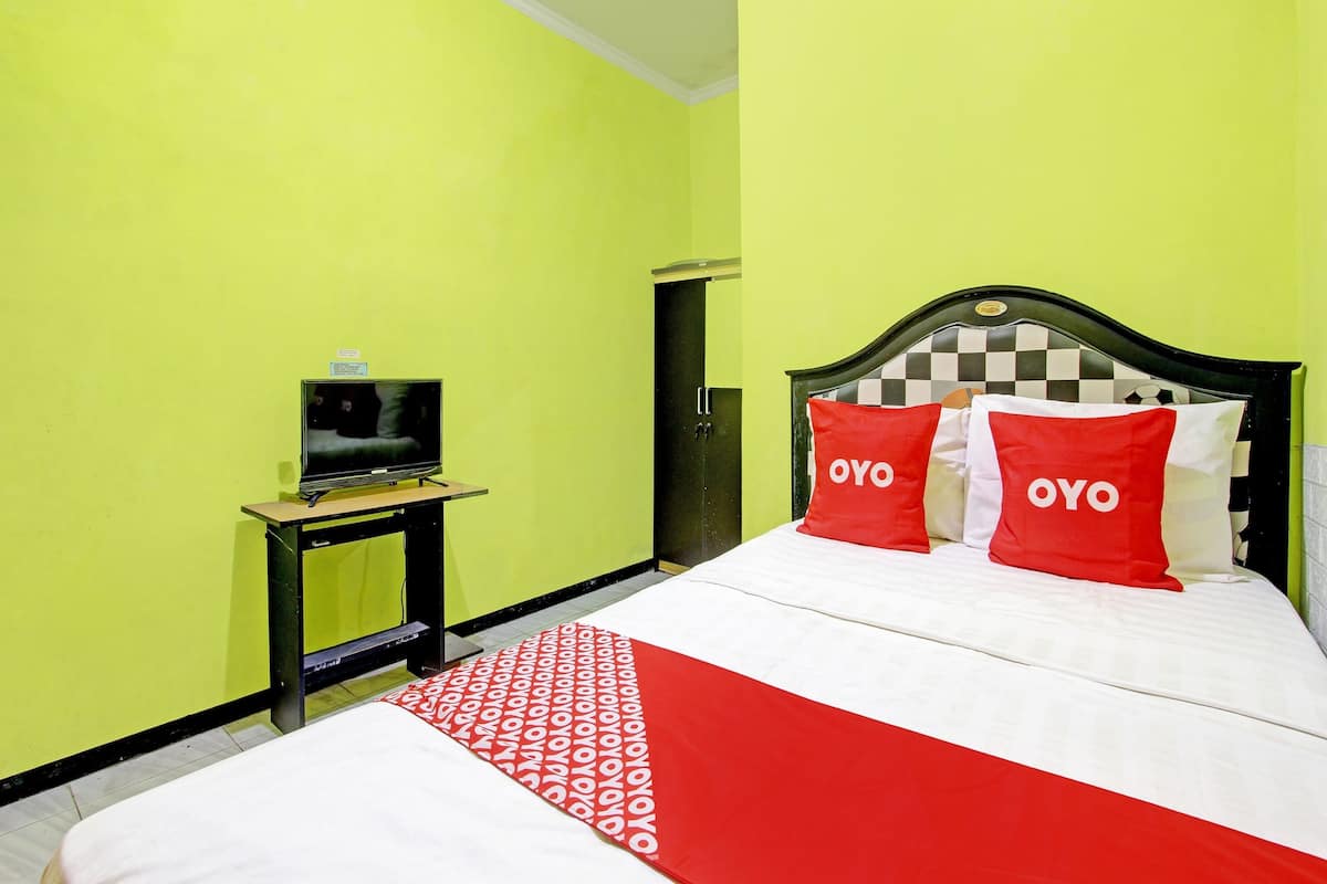 A hotel room with a bed, a TV on a small table, and a wardrobe.