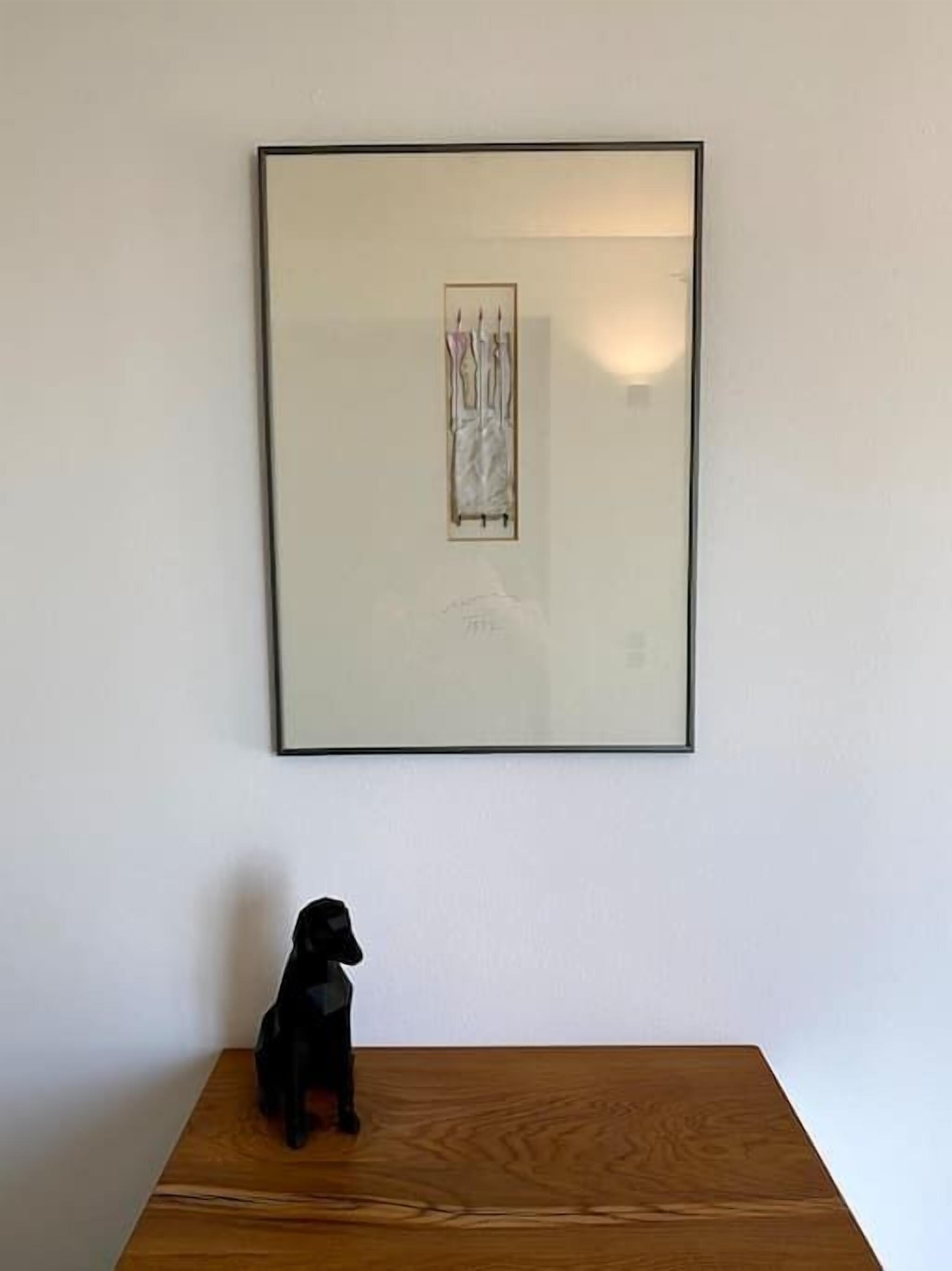 Una obra de arte enmarcada en una pared, sobre una mesa de madera donde descansa un perro negro.