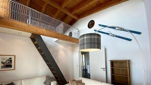 A modern living room with a white sofa, a staircase, and a loft area with a mesh ceiling.
