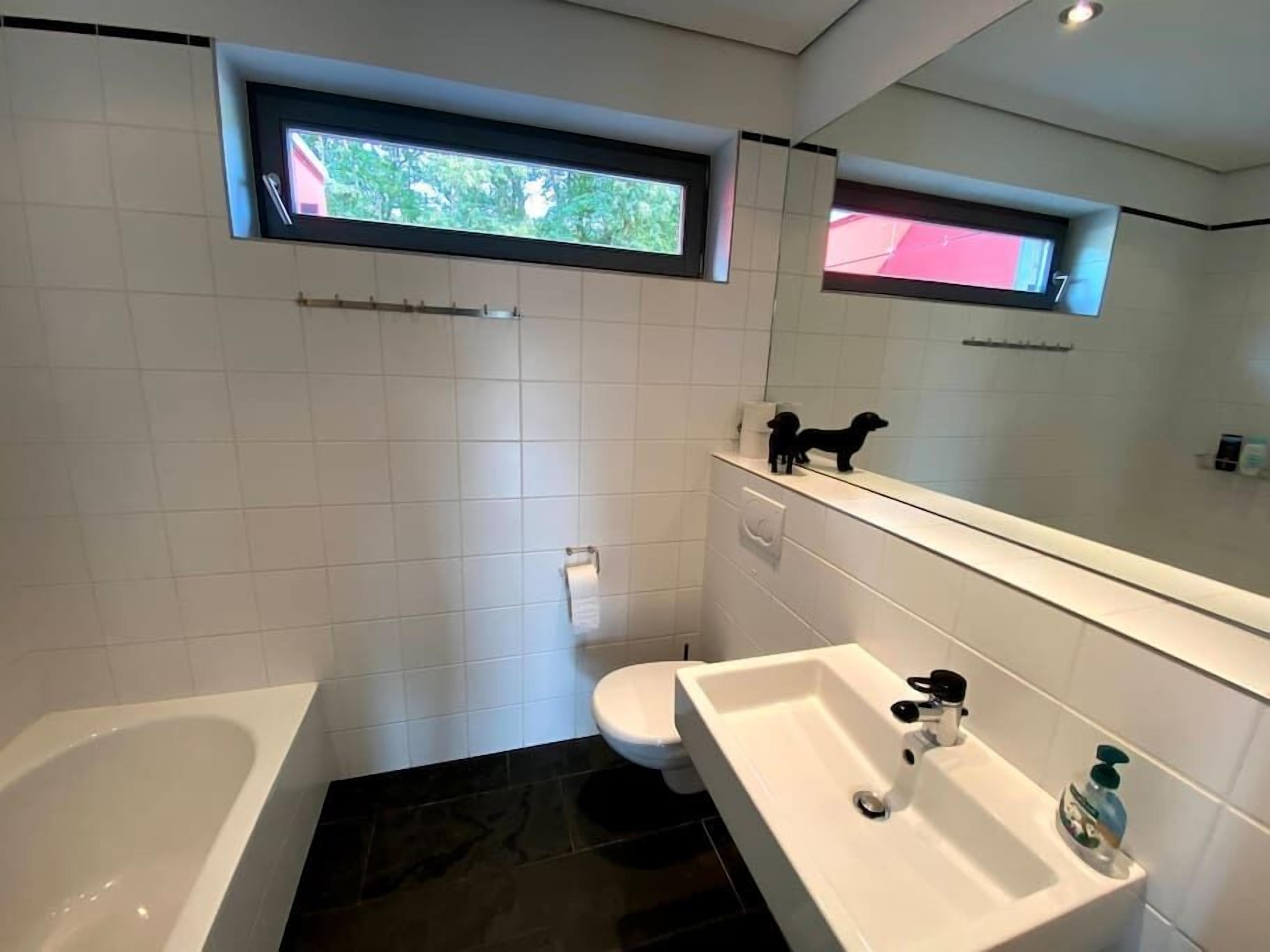 Un bagno moderno con vasca, water e lavandino. Si vede una finestra sopra il water e uno specchio sopra il lavandino.