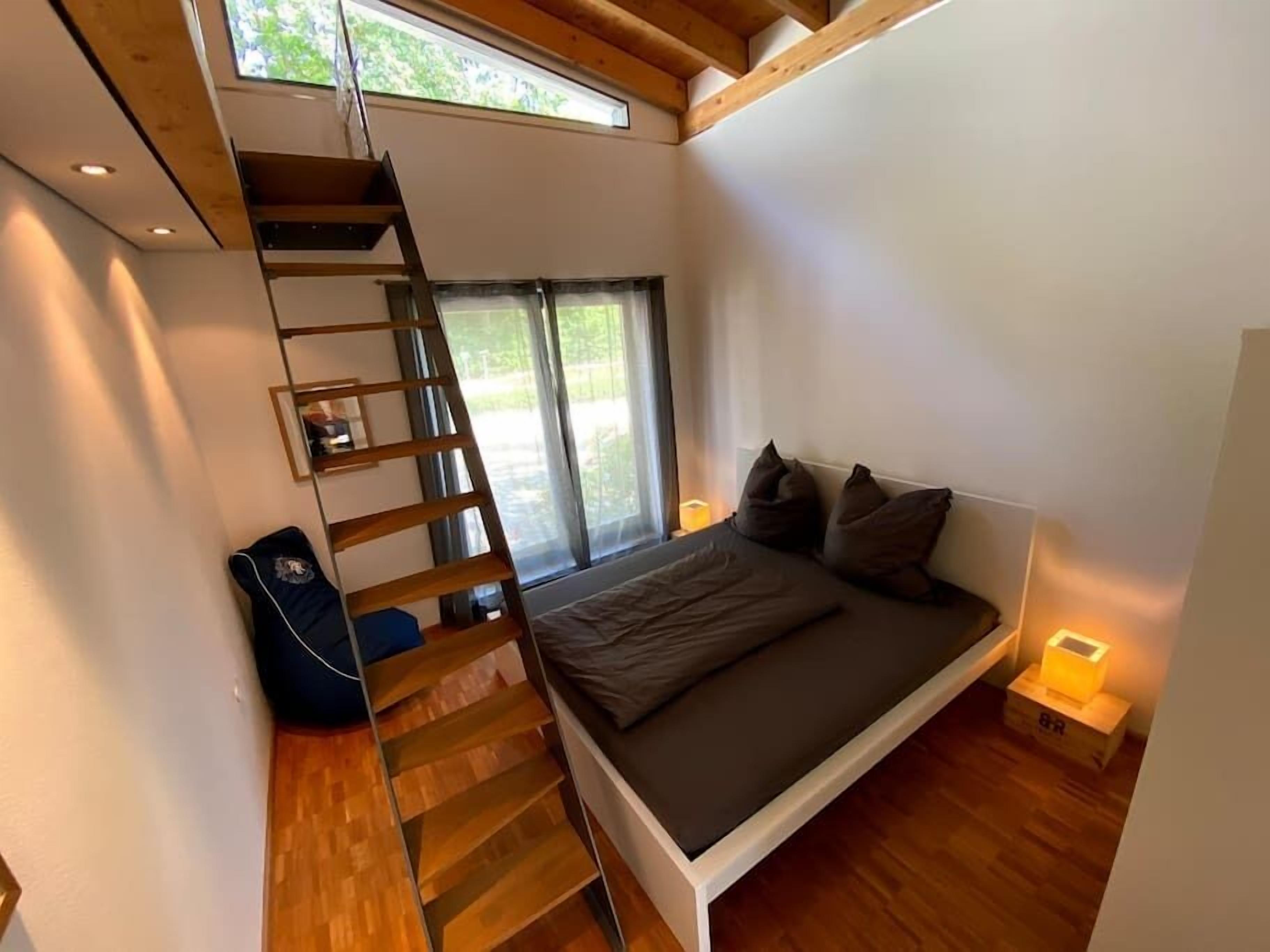 A bedroom with a bed, a wooden ladder, a window, and a small bedside table.