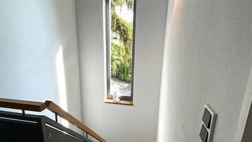 Eine Treppe mit Holzdielen und einem schwarzen Geländer, die zu einer Zwischenebene mit einem kleinen Fenster mit Blick auf Grün führt.