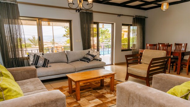 A living room with a sofa, armchairs, a coffee table, and a dining area with chairs. - Stunning 3-bed House in Kigali (Kigali)