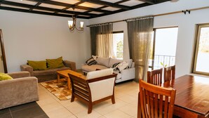 A living room with a sofa, a wooden bench, a dining table with chairs, and a view of the outdoors through a window. - Stunning 3-bed House in Kigali (Kigali)
