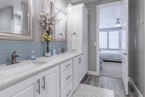 Une salle de bain moderne avec un double vasque, des meubles blancs, un grand miroir et un vase de fleurs.