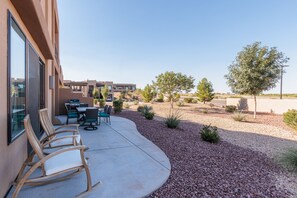 Un espace patio aménagé avec du mobilier d’extérieur, un sol en béton et un jardin paysager agrémenté de petits arbustes et d’arbres.