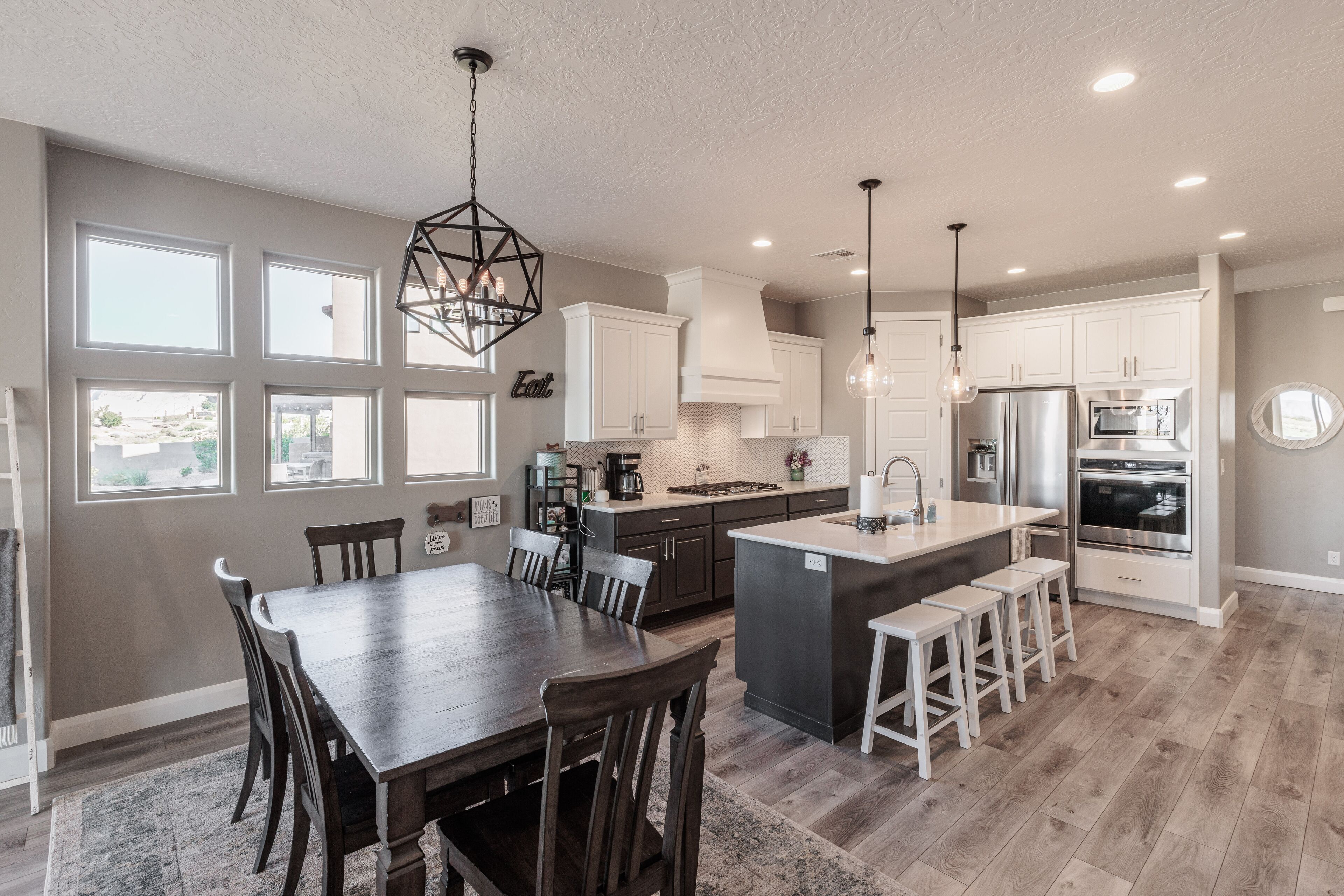 A modern kitchen with a central island, white cabinetry, and a dining area with a dark wooden table and chairs.