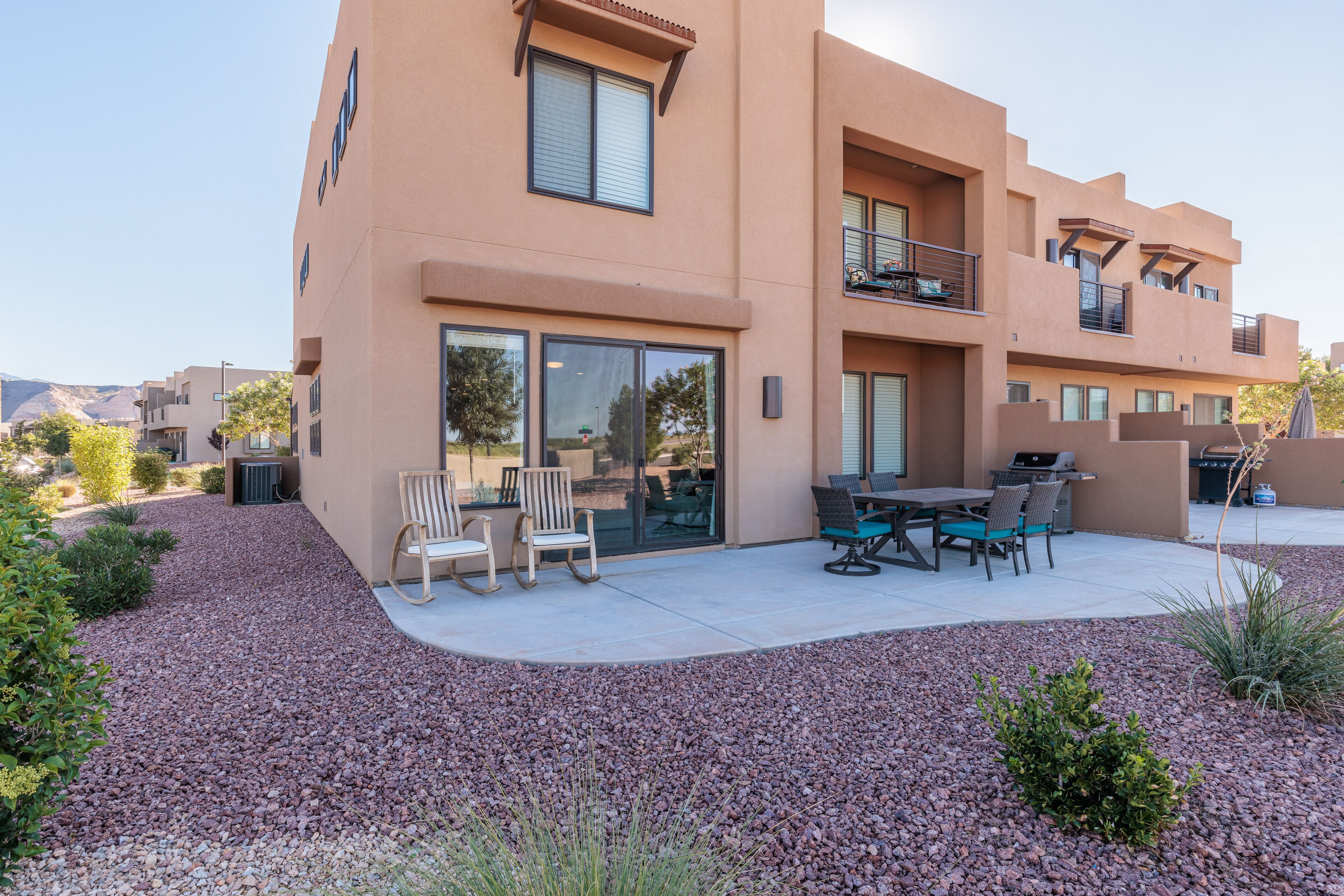 A modern two-story building with a patio area featuring outdoor furniture and a barbecue grill.