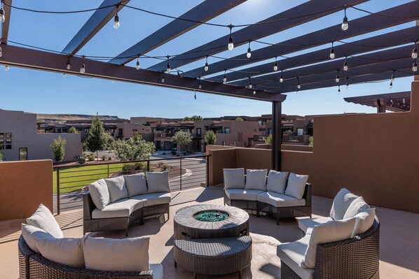 Un espace extérieur aménagé en terrasse, avec des meubles en osier, un foyer et des guirlandes lumineuses.