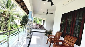 Un balcon spacieux avec deux chaises en bois, une rambarde en verre et des ventilateurs de plafond.