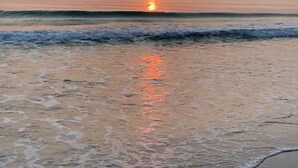 Une plage où les vagues viennent doucement lécher le rivage, avec un coucher de soleil en toile de fond.