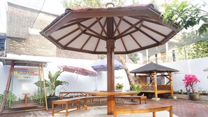 An outdoor seating area with wooden tables and benches, a central umbrella, and a decorative gazebo. - Hotel O Trisna Patihan Resort (Tulungagung)
