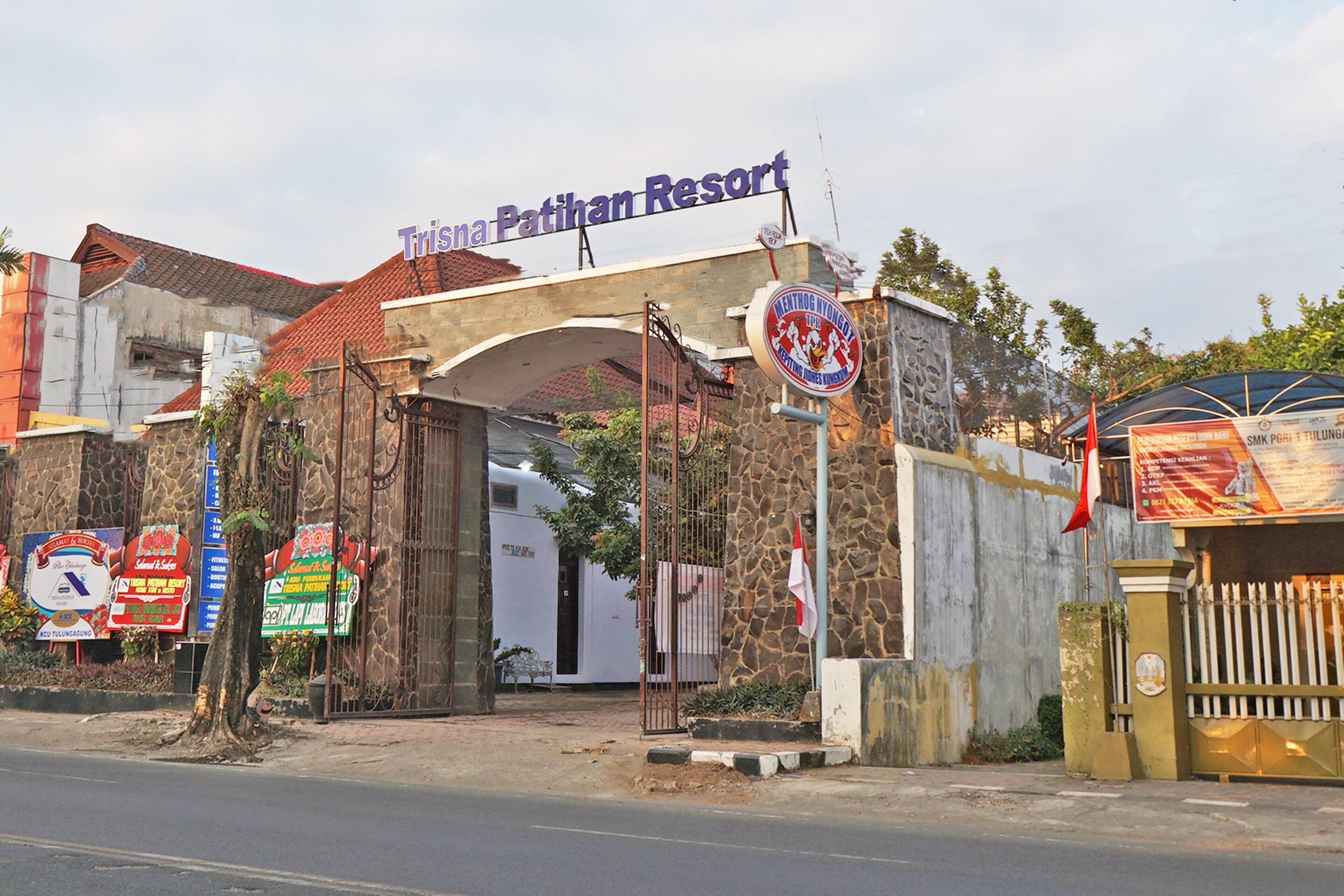 La entrada al Trisna Patihan Resort, con fachada de piedra, una puerta metálica y varias indicaciones.